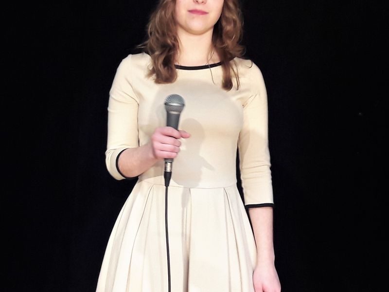 Na zdjęciu wokalistka MCK - Julianna kołodziejczyk. Wokalistka w sukni z mikrofonem w ręku