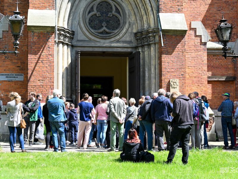 Na zdjęciu grupa uczestników spaceru śladami tomasowskich ewangelików. Grupa stoi przed wejściem głównym do kościoła ewangelickiego Zbawiciela przy ul. Św. Antoniego