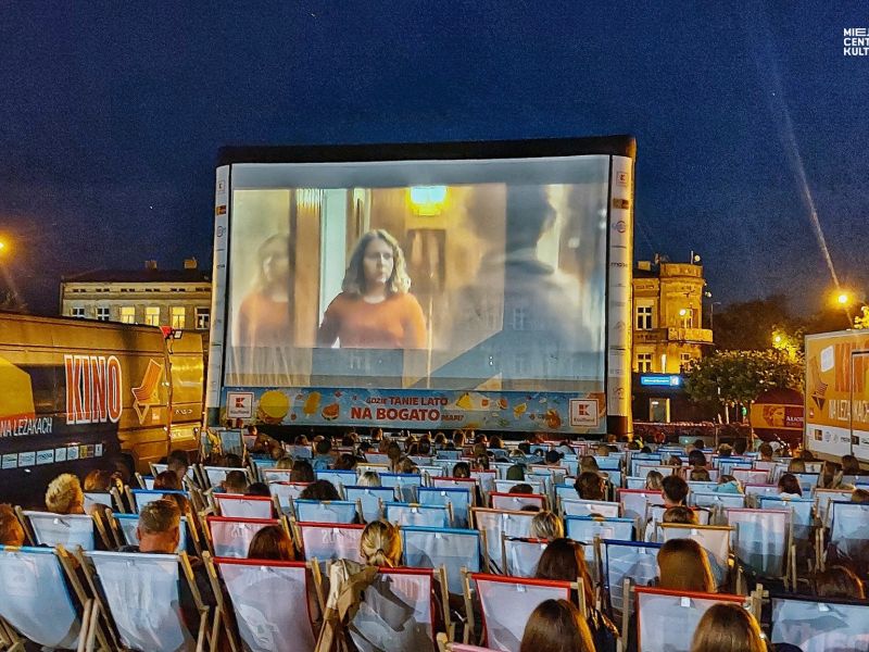 Na zdjęciu seans w ramach Kino na leżakach, projekcja filmu na placu Kościuszki. Widzowie siedzą na leżakach i oglądają seans wyświetlany na duuzym, plenerowym ekranie