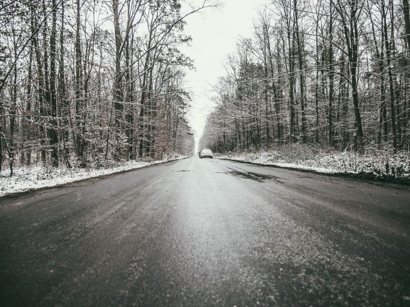 Na zdjęciu oblodzona nawierzchnia drogi podczas przymrozku. Po bokach drogi obśnieżone drzewa (las)