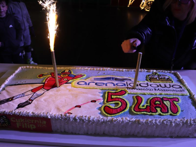 Na zdjęciu tort z okazji 5 urodzin Areny lodowej. Na torcie pali się raca świetlna oraz znajduje się okolicznościowe zdobienie