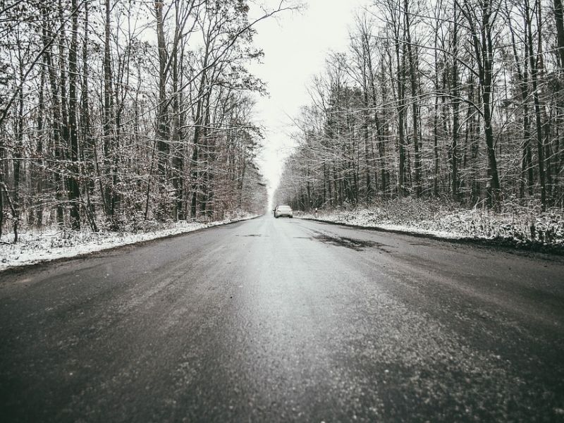 Na zdjęciu marznące opady na drodze. Widac auto, droga przebiega przez las
