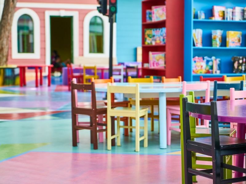 Na zdjęciu sala przedszkolna wyposażona w kolorowe stoliki i krzesełka i półki z zabawkami