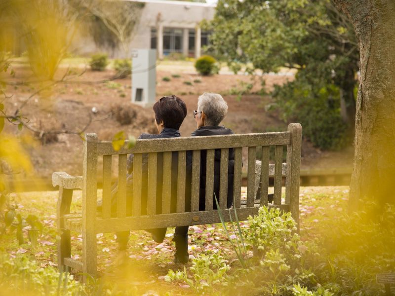 Na zdjęciu dwójka seniorów siedząca na ławce, aura jesienna
