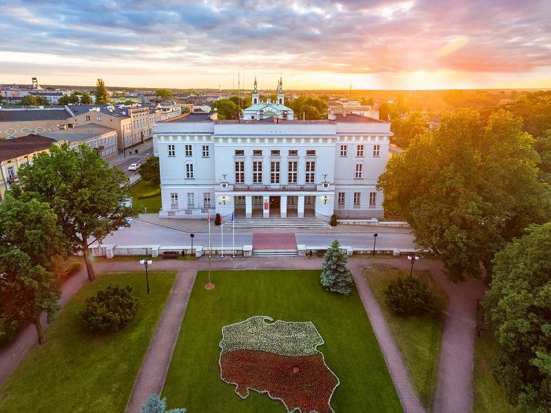 Na zdjęciu gmach Urzędu Miasta w Tomaszowie Mazowieckim sfotografowany przez drona. Przed gmachem na trawniku klomb w kształcie konturów Polski