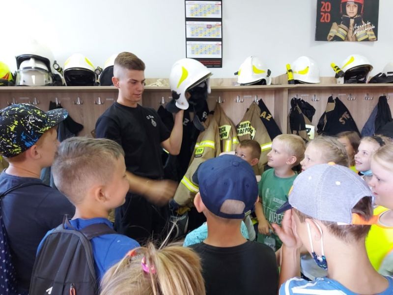 Na zdjęciu dzieci z pólkolonii na spotkaniu w Ochotniczej Straży Pożarnej. Strażak demonstruje im chełm strażacki