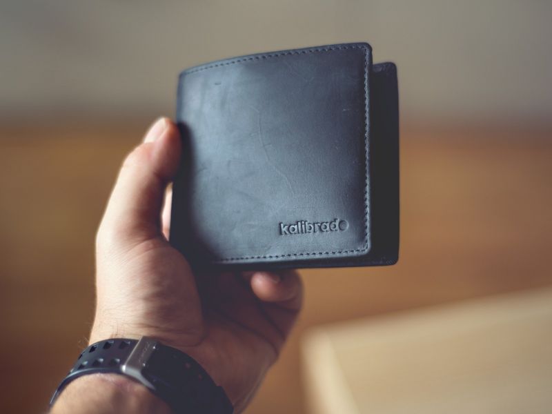 Na zdjęciu ręka trzymająca portfel koloru czarnego