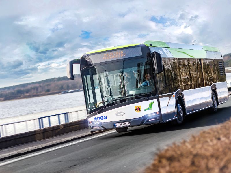 Zdjęcie przedstawia autobus MZK, za szybą przednią widovczny kierowca, autobus przejeżdża przez tamę Zalewu Sulejowskiego