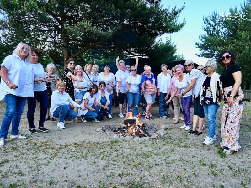 Na zdjęciu grupa seniorów przy ognisku z kiełbaskami na kijach
