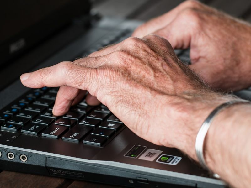Na zdjęciu ręce seniora na klawiaturze laptopa