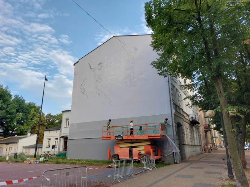 Na zdjęciu szkic muralu, który powstaje na kamienicy przy ul. Św, Antoniego. Widać bok kamienicy oraz podnośnik i pracujące przy muralu osoby