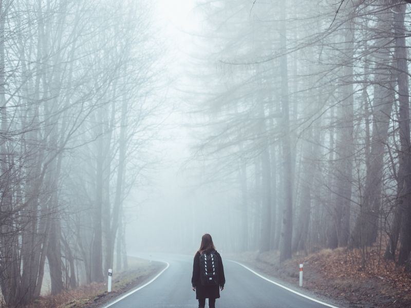 Dziewczyna stoi na dordze asfaltowej w lesie, duża mgła