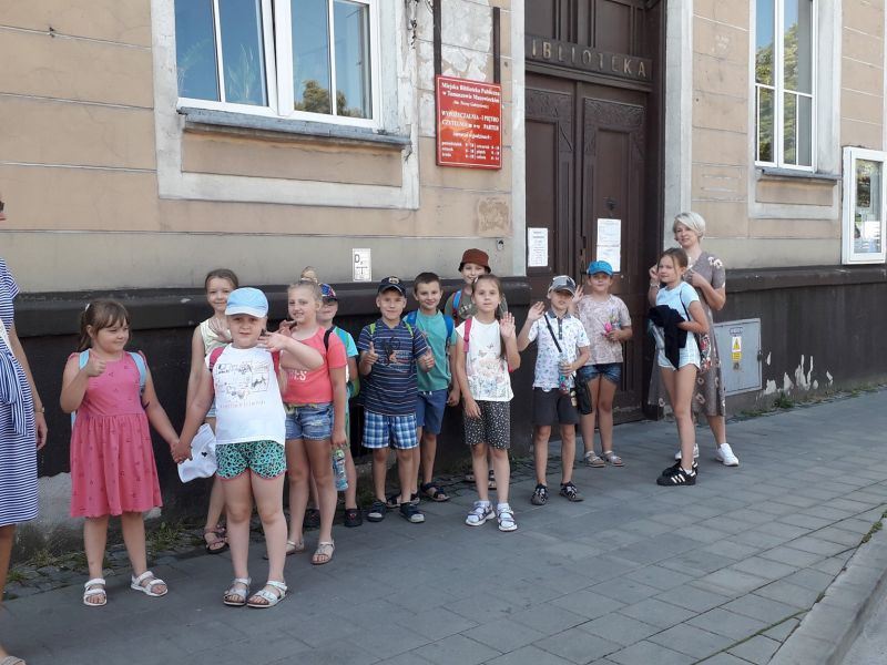 Na zdjęciu uczestnicy warsztatów bibliotecznych przed budynkiem MBP. Dzieci w strojach półkolonijnych i dwie wychowawczynie