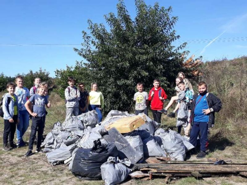 Na zdjęciu uczniowie ze szkoły podstawowej, w tle zebranych w worki śmieci, które zostały zebrane i sprzątnięte z lasu 