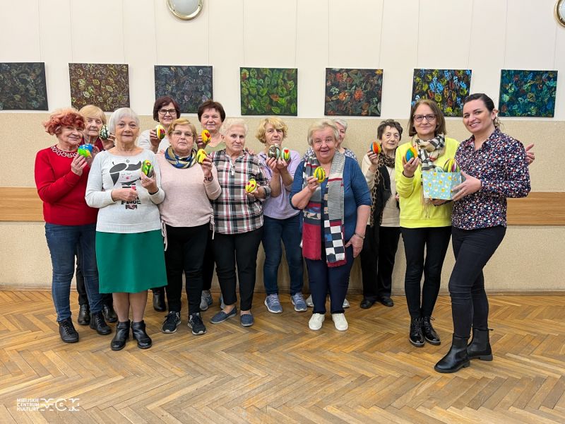 Na zdjęciu seniorzy, którzy wzięli udział w warsztatach dla seniorów w MCK Za Pilicą. Zdjęcie grupowe, seniorzy demonstrują wykonane na warsztatach jajka wielkanocne z filcu
