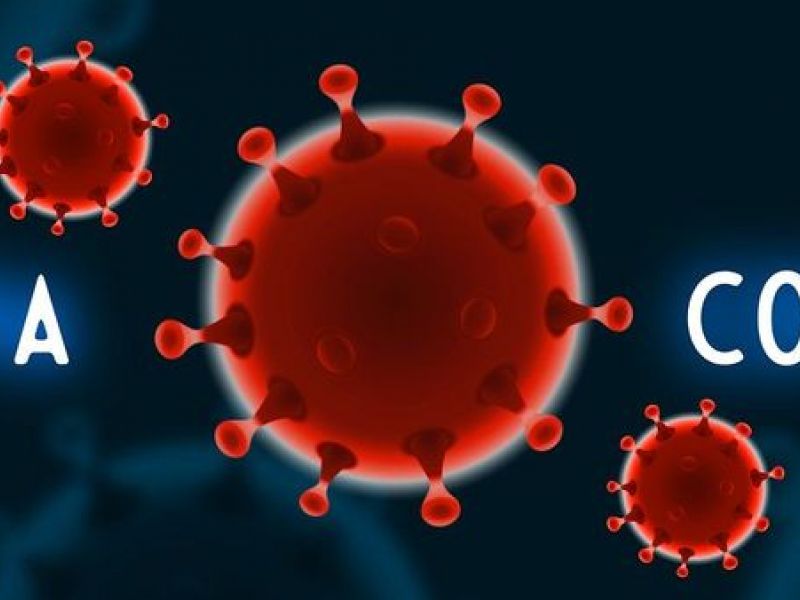 Na zdjęciu baner z grafiką komórki koronawirusa w kolorze czerwonym na niebieskim tle. Białymi literami napis: COVID-19
