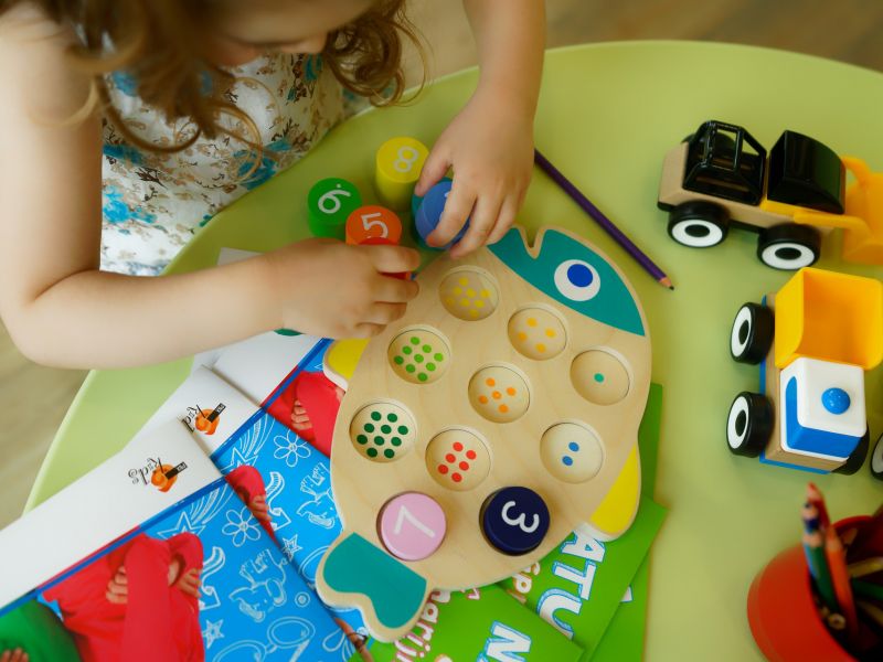 Na zdjęciu mała przedszkolanka bawi się klockami rozłożonymi na stoliku