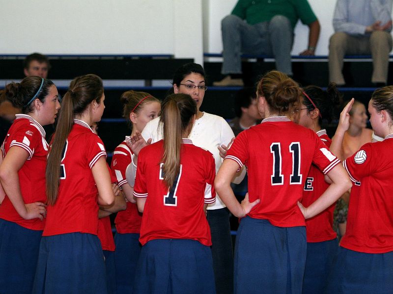 Na zdjęciu zawodniczki w czerwonych koszulkach konsultują stan meczu z trenerką w białej koszulce i w okularach