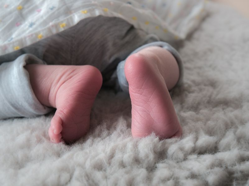 Stopy niemowlaka w szarym body na puchatym białym kocu 