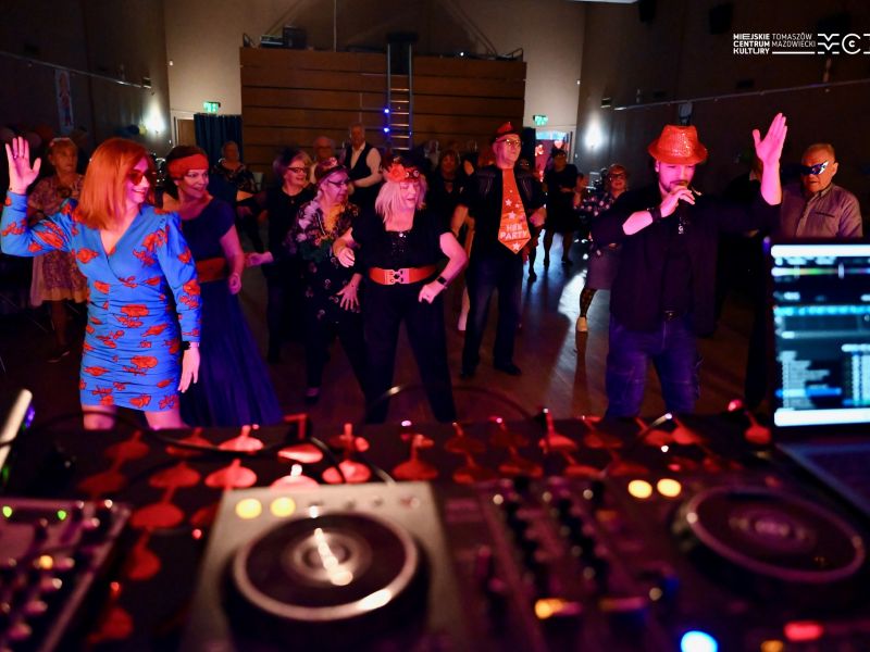 Na zdjęciu DJ prowadzący zabawę senioralną. W tle osoby tańczące
