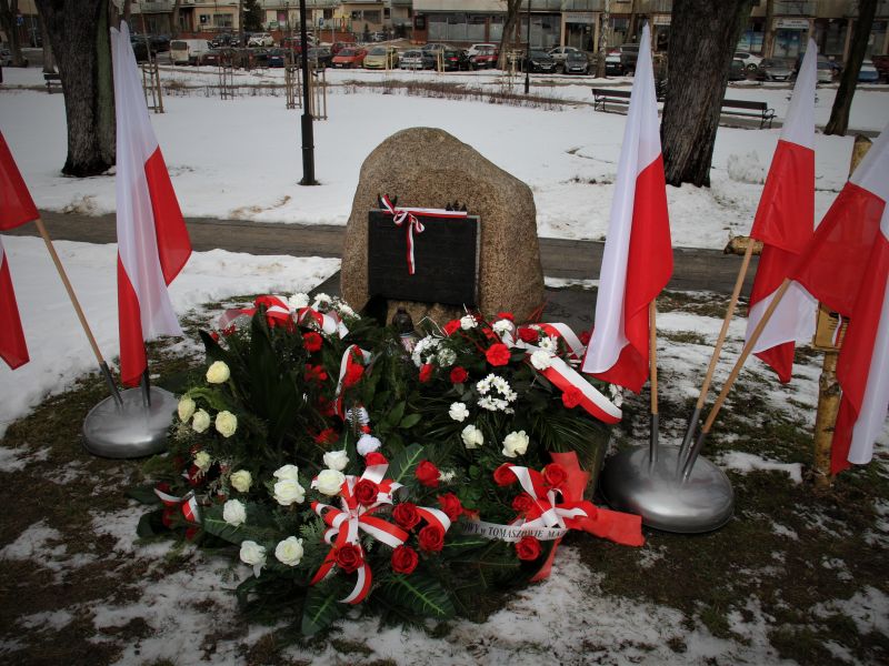 pomnik w  otoczeniu flag oraz biało czerwonych wieńcy