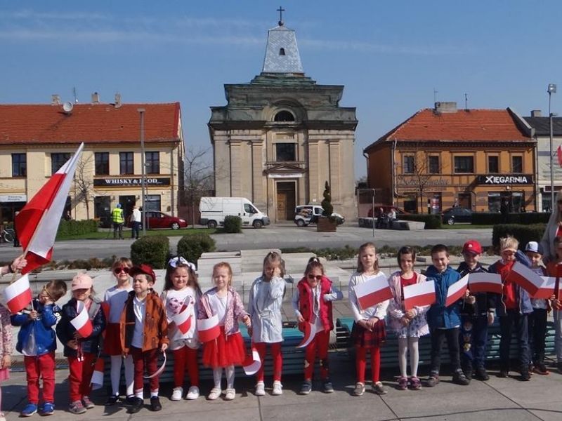 Zdjęcie przedszkolaków z Przedszkola nr 7 na obchodach Dnia Flagi. Dzieci pozują na placu Kościuszki z biało-czerwonymi chorągiewkami