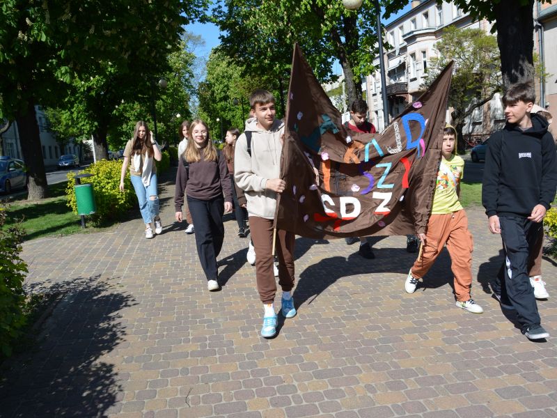 Na zdjęciu uczniowie podczas rajdu pieszego ulicami Tomaszowa Mazowieckiego. Niosą baner z nazwą rajdu.