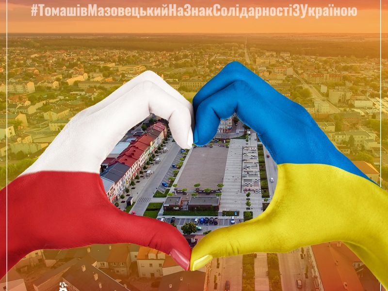 Na zdjęciu złożone w kształt serca dłonie w barwach Ukrainy. W tle panorama Tomaszowa Mazowieckiego