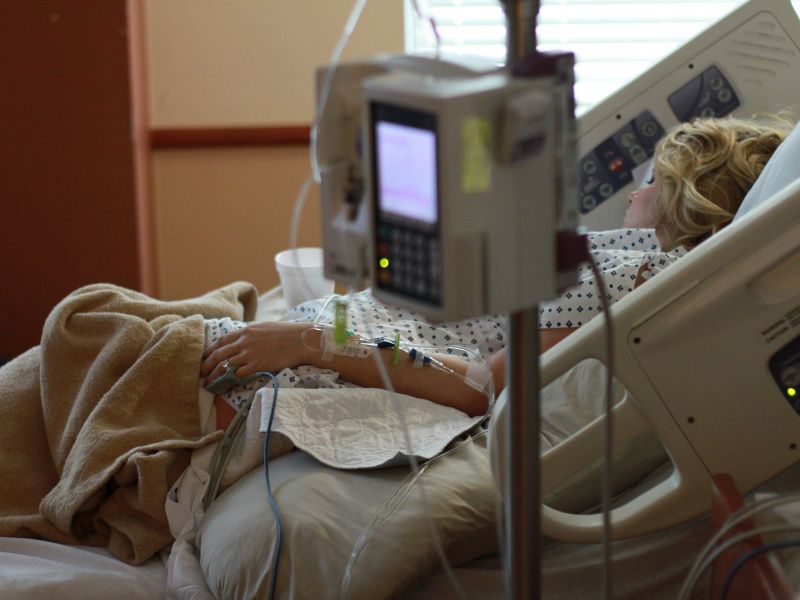 Zdjęcie ilustracyjne, kobieta leży w łóżku szpitalnym, obok niej stoją medyczne urządzenia