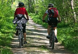 Na zdjęciu dwójka rowerzystów na ściezce rowerowej w lesie
